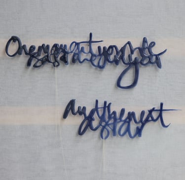 A glass sculpture with semi-abstract text hangs on a wall. its 2 sections are joined by silver chain