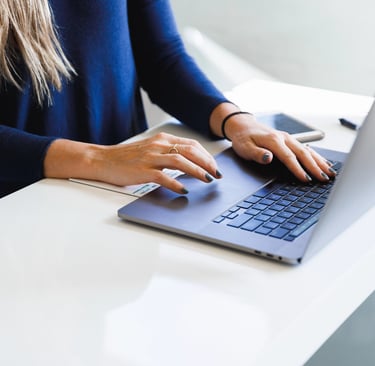 Femme habillée en bleu assise à son bureau blanc et qui pianote sur son ordinateur portable