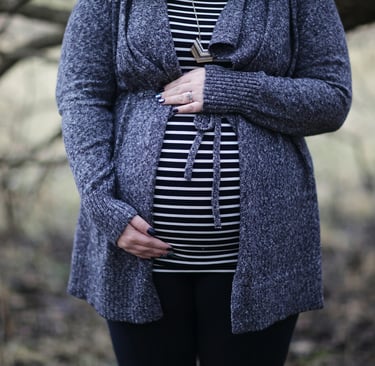 a pregnant woman wearing a striped shirt and a blue cardigan holding her belly