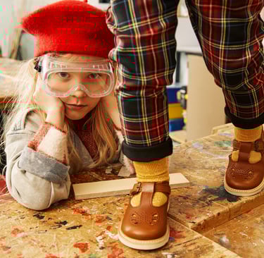 A young girl with a red beret and lab goggles, and a child on a table wearing Young Soles shoes