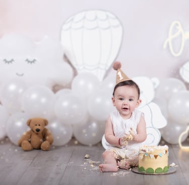 un bebé que acaba de cumplir 1 año de edad, con sombrero de fiesta, un osito de peluche y un pastel