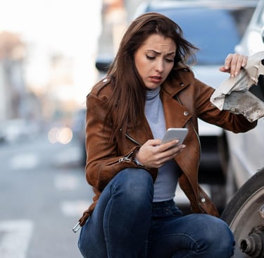 a woman in a leather jacket is looking at her phone phone after having a car crash