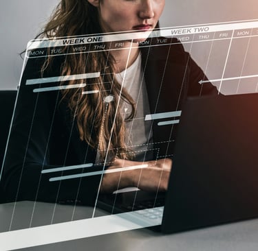 a woman sitting at a desk with an open laptop, working on a calendar