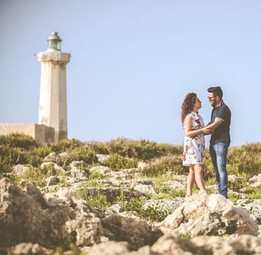 una coppia in piedi su una spiaggia rocciosa con un faro sullo sfondo