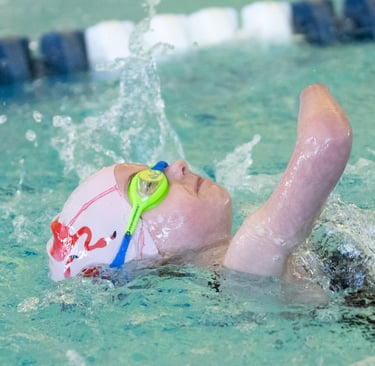 Young girl swimming on her back in pink swim cap with flamingos and blue and green goggles