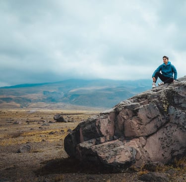 Fotografía de retrato profesional de aventura de un joven sentado en la cima de una roca en un paisaje hermoso de montaña