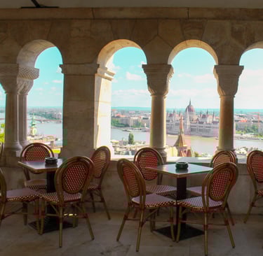 veduta del parlamento di budapest attraverso una terrazza con tavolini e protetta da piccoli archi 