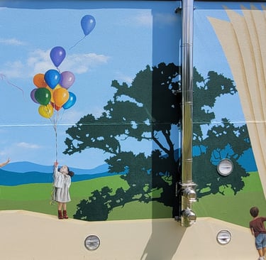 Fresque peinte sur façade. Des enfants jouent sur un muret, un paysage simplifié en arrière plan.