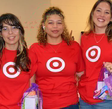 three women in red shirts are standing in a room holding hygiene kits