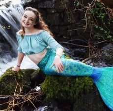 Mermaid Echo wearing a blue tail. She is sitting on a rock.