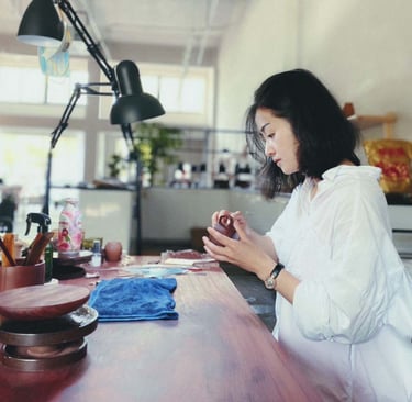 Artisan seated at a workbench, holding a Zisha teapot and examining it closely