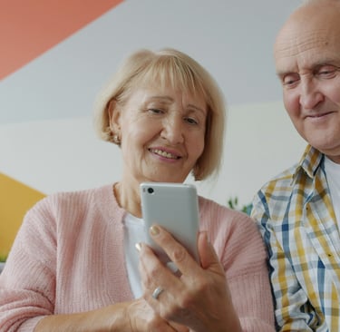 A happy senior couple sitting together on a couch while using a smartphone for a active aging
