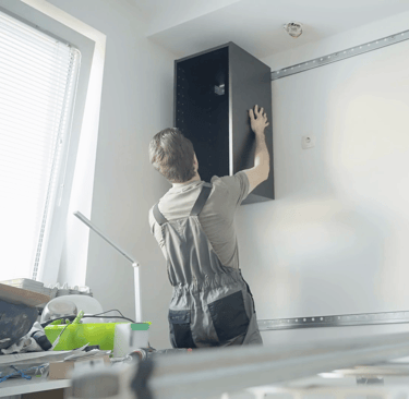 Mężczyzna montuje korpus szafki wiszącej za pomocą listwy montażowej 