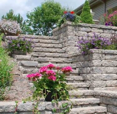 Landscaped block retaining wall with stone steps and plants