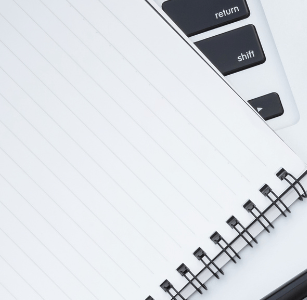 a laptop computer and a notebook with a notepad and a pen