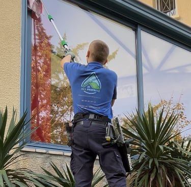 Un personne qui nettoie une vitre en hauteur à l'aide d'une perche