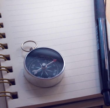 A compass on top of a notebook, with a pen and camera on the side
