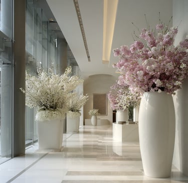 Elegant modern hotel lobby hallway featuring large white floor vases with pink and white floral cherry blossom arrangements.