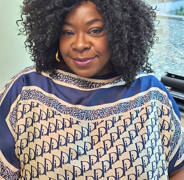 Smiling woman with voluminous curly hair wearing a blue and white patterned designer tunic top.
