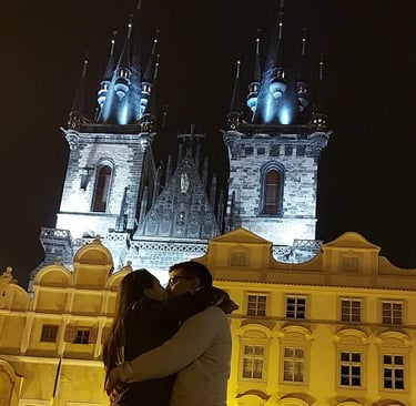 Pareja abrazándose frente a la Iglesia de Týn iluminada por la noche en Praga.