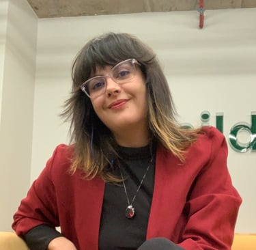 Josi sorrindo e vestida de preto com terno vermelho, cabelos soltos e óculos transparente.