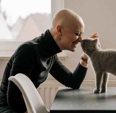 Bald woman in a turtle neck is petting her grey cat and getting acupuncture for cancer side effects