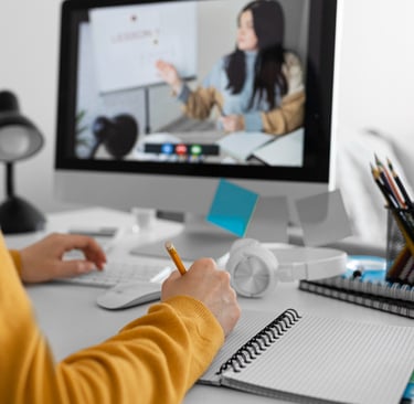 Seorang pelajar mengikuti sesi pembelajaran online dan mencatat materi sambil melihat kelas virtual di layar komputer.