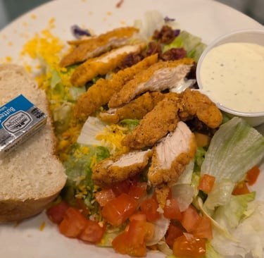 salad with friend chicken on top with ramekin of ranch and bread
