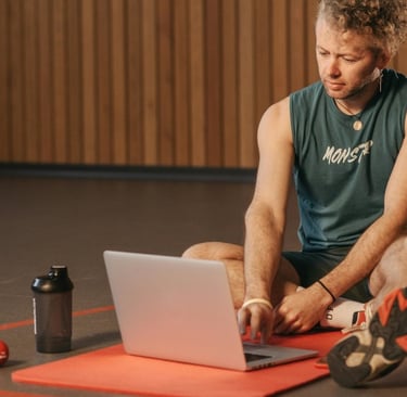 a man sitting on a mat with a laptop computer