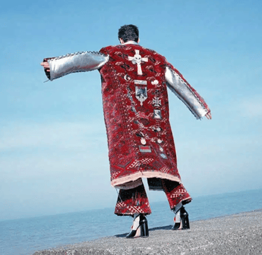 Back view of couture red embroidered coat styled against coastal backdrop.