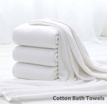 a stack of Cotton Bath towels and towels on a bed
