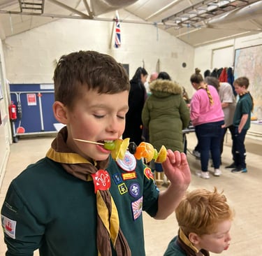 A cub from the 25th Allerton eats some fruit on a stick.