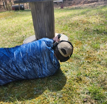 Man laying on side engaging targets from a barrier using self-defense firearm during training.