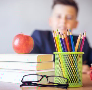 a boy sitting at a table with an apple, book, pencils and glasses