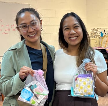 two women standing next to each other in a room holding hygiene kits