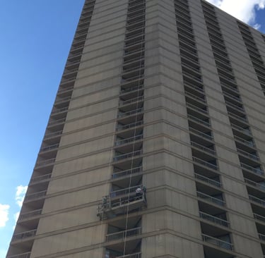 Concrete facade restoration on a tall skyscraper using a suspended work platform.