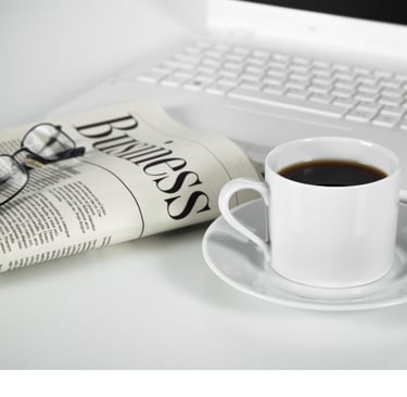 Pic of a folded newspaper with glasses on top, a mug of coffee, and a laptop