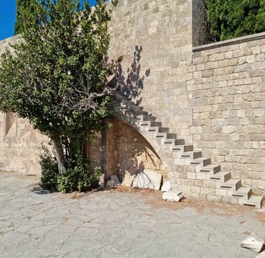 Ancient stone steps built into a medieval fortress wall next to a green tree in Rhodes, Greece.