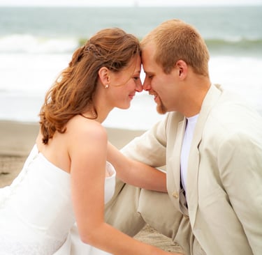 bride and groom, beach photoshoot, sand, ocean, bouquet, sitting