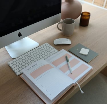 a desktop with an apple computer, coffee and a planner.