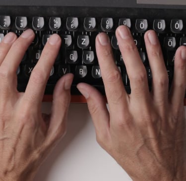 Hands typing on an orange and black typewriter with a blank sheet of paper.