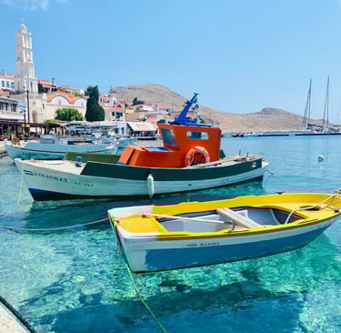 Traditional fishing boats floating on clear turquoise water at the scenic harbor of Halki Island in Greece.