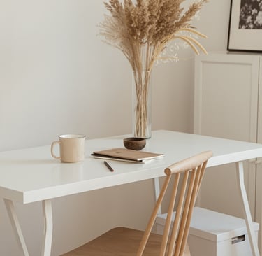 Photo of work desk, with vase of pampas grass and mug, notebooks and chair in neutral tones