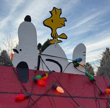 Lawn decoration of Snoopy and Woodstock on a red dog house wrapped in Christmas lights