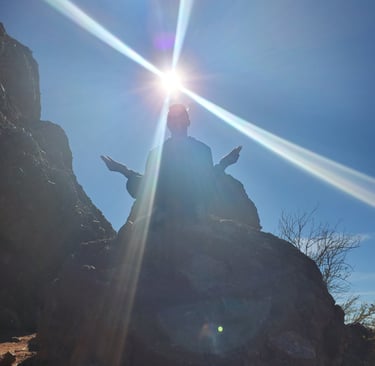 The silhouette of a person on a mountain meditating with the sun in the background.
