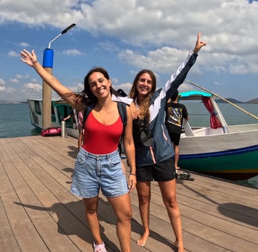 two women standing on a wooden deck with a boat in the background, Snorkeling & Keliling Pulau Gili 