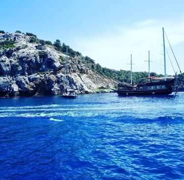 A wooden pirate ship and a sailboat anchor in the bright blue water of a Mediterranean bay.