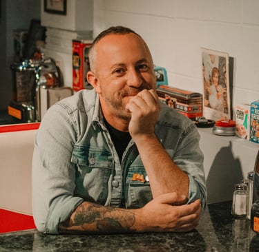 Photo of Dan Clapson sitting in a diner booth, taken in Calgary by Annie da Silva