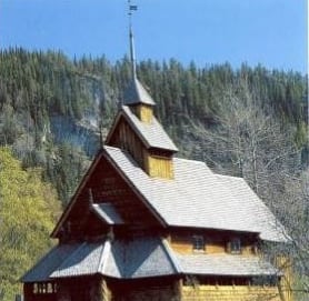 A wooden stave church with pine trees in the background