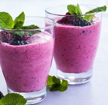 Two glasses with purple smoothie inside, mint leaves and blackberries garnish